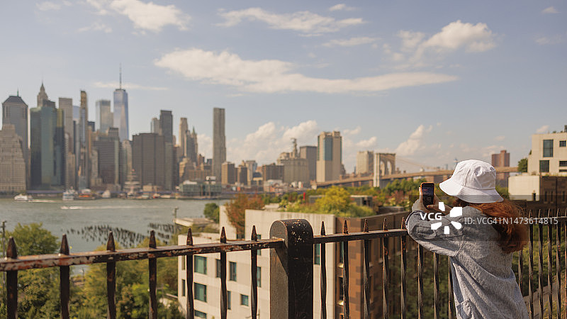 在布鲁克林高地长廊拍摄曼哈顿世贸中心一号大楼的年轻女子图片素材