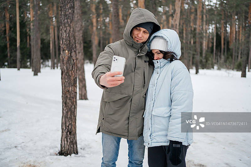 春季雪林野餐，一家人在智能手机上自拍合影图片素材