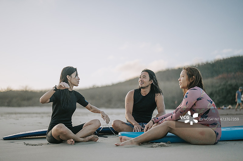 亚洲中国朋友在海上冲浪后坐在海滩上休息图片素材