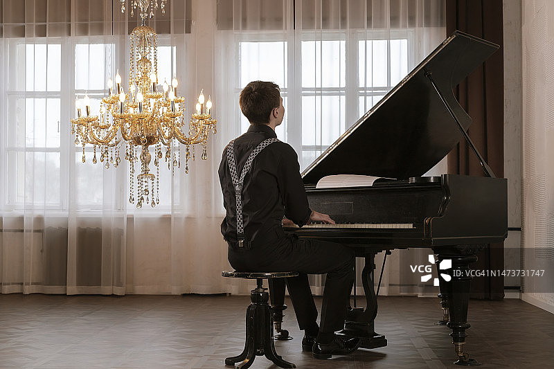 身穿黑色西装和吊带的英俊年轻男人在弹钢琴（背面视角）图片素材