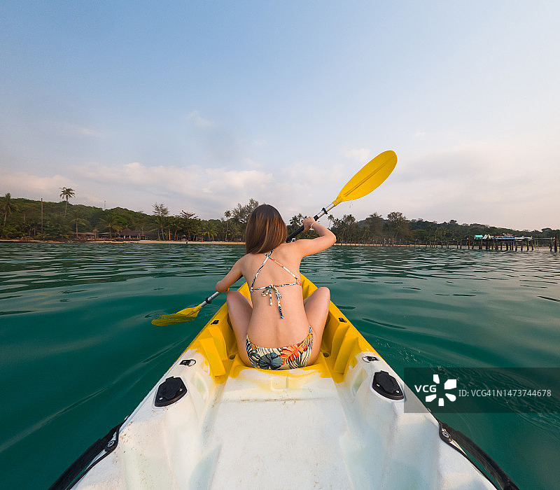 比基尼女郎在平静的海面上划皮划艇的背影图片素材