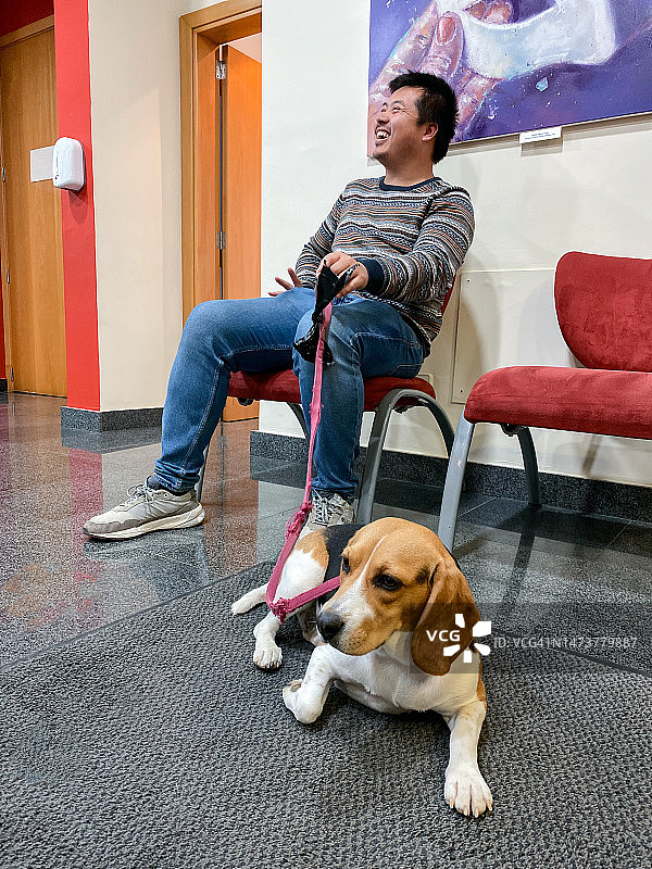 年轻的亚洲男人和他的比格犬一起笑着等待去看兽医图片素材