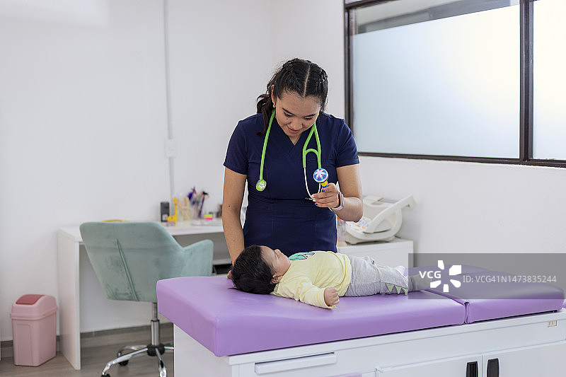 儿科医生在诊所里给婴儿看拨浪鼓图片素材