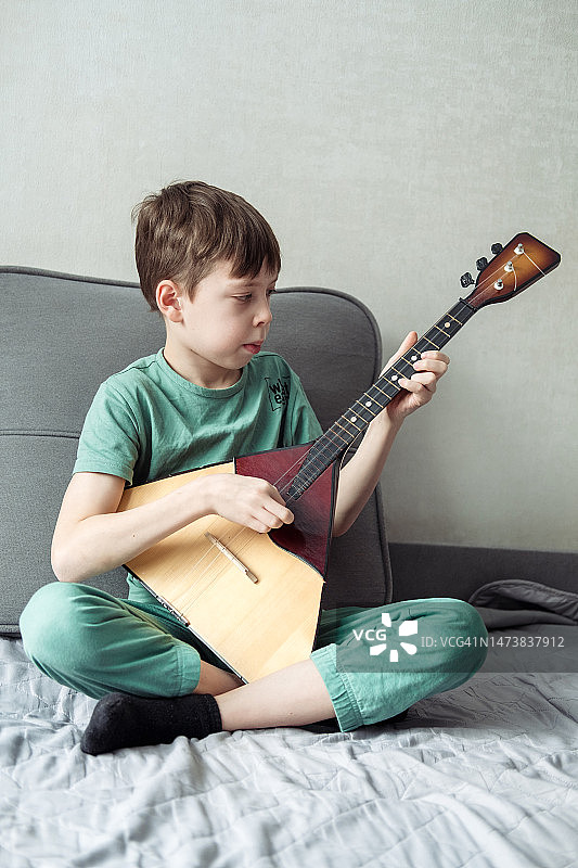 青少年在家里的沙发上弹奏巴拉莱卡琴图片素材