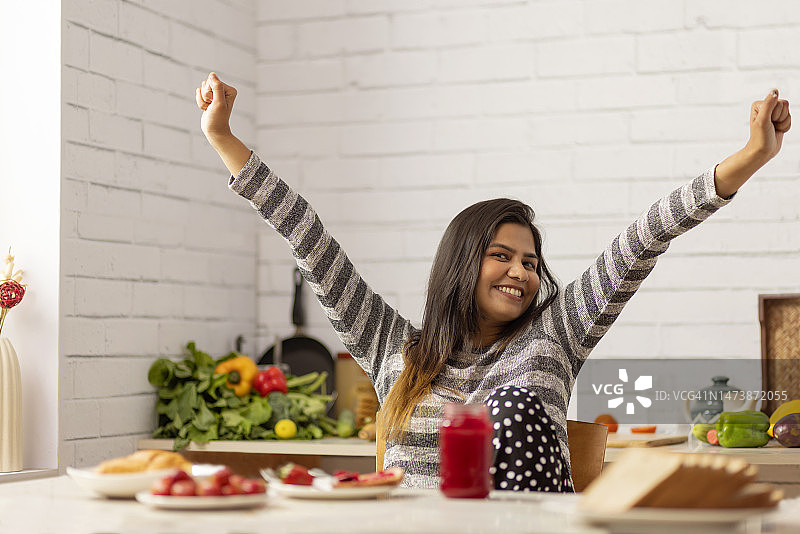早餐时在厨房里举起双臂的快乐女人图片素材