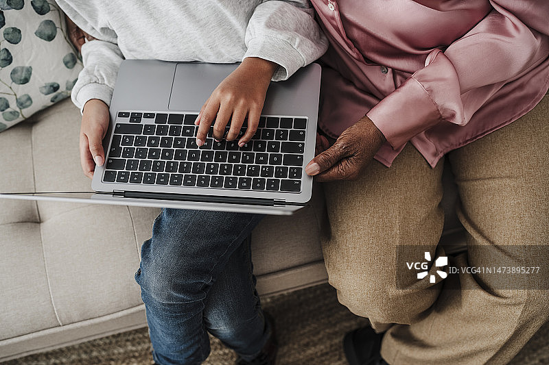 女孩在家使用笔记本电脑，祖母坐在沙发上图片素材