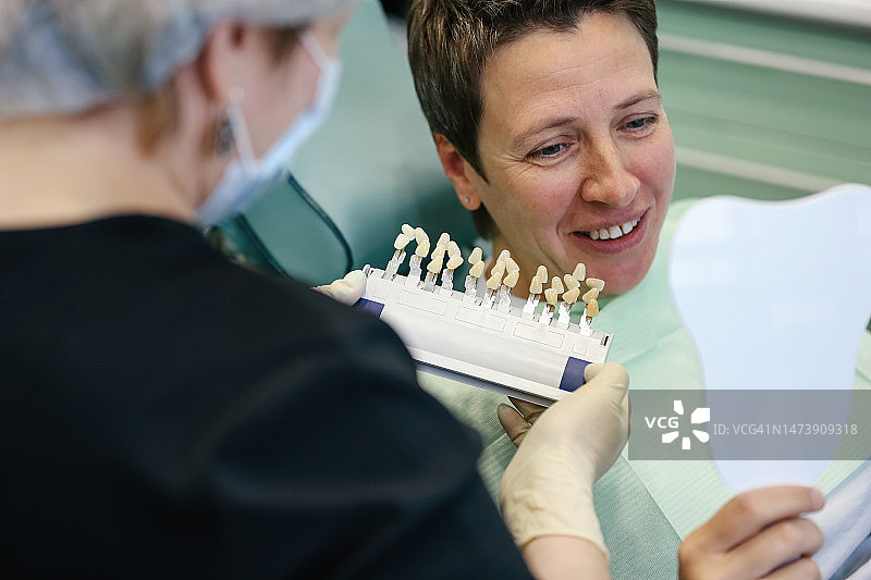 女牙科医生和中年妇女使用镜子和牙齿颜色图表进行种植牙图片素材