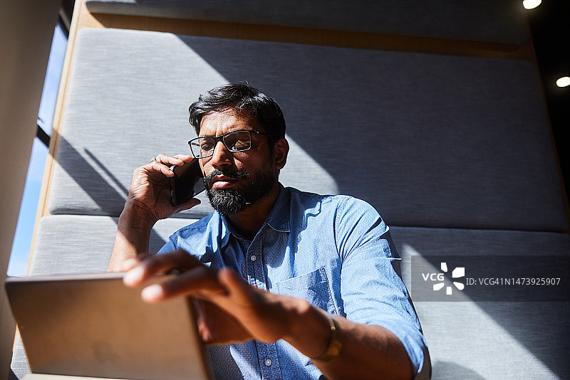 商人一边在办公室隔间里用平板电脑工作一边打电话图片素材