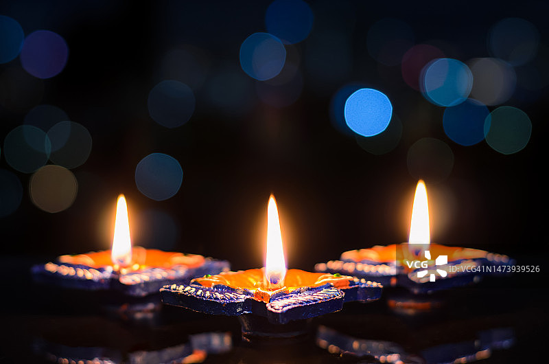 在深色背景上点燃的第一个泥土油灯火焰特写，带有彩色散景灯图片素材