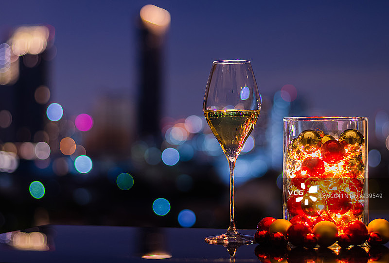 彩色城市背景下装有圣诞装饰品和灯饰的玻璃花瓶中的单杯白葡萄酒图片素材