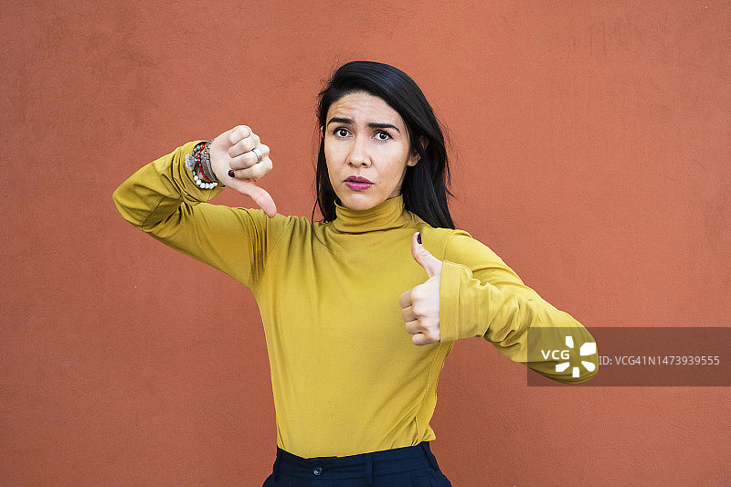 困惑地看着镜头并竖起大拇指的拉丁裔女性图片素材