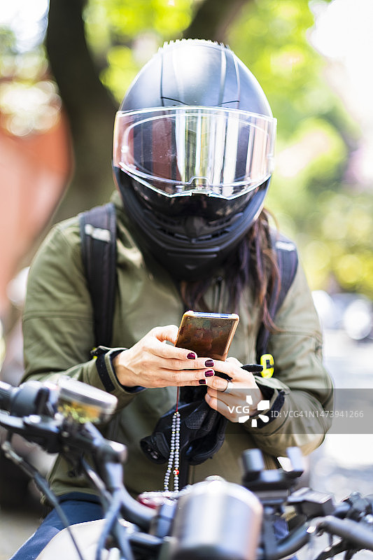坐在墨西哥城摩托车上看着手机的拉丁裔女性，中景图片素材