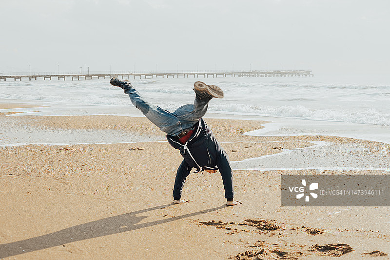 在俄罗斯，年轻男人在冬季的沙滩上用手做翻筋斗图片素材