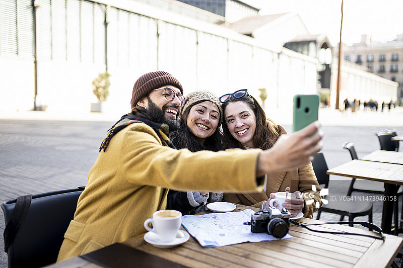 三个快乐的朋友在阳光明媚的户外咖啡馆自拍图片素材