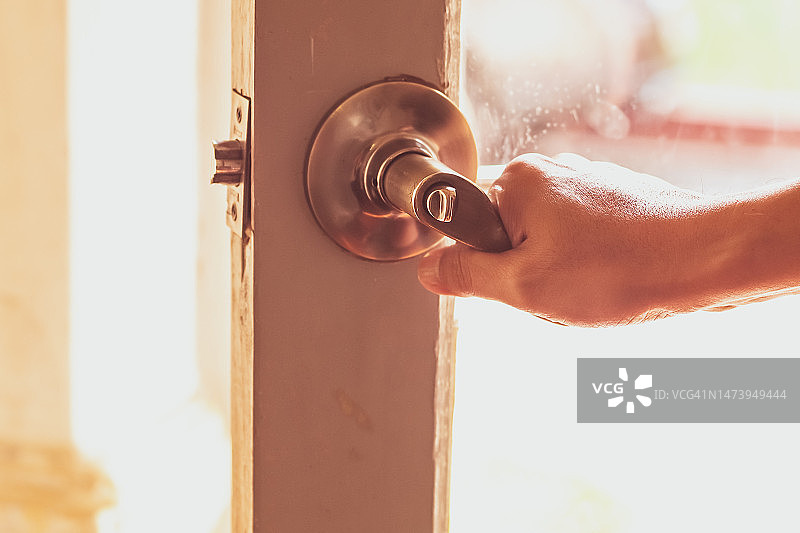 男子开门，手和门把手的特写，光线穿过玻璃图片素材