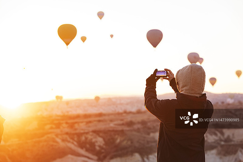 成年男人在卡帕多奇亚用手机拍摄热气球图片素材