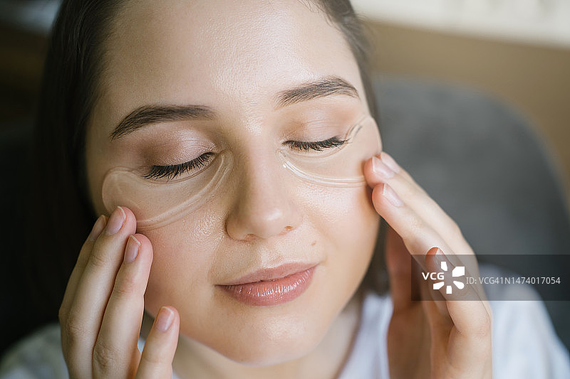在皮肤上涂抹眼部凝胶贴的年轻女子面部特写图片素材