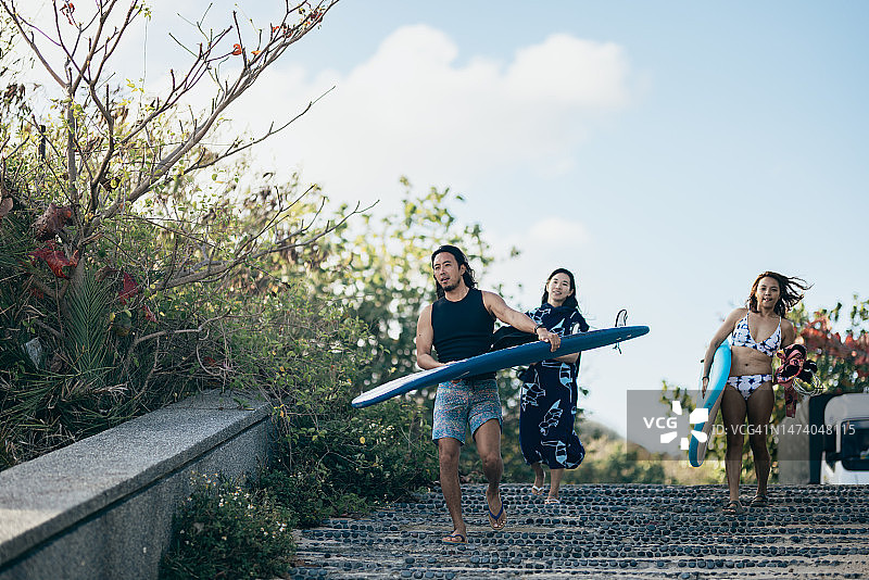 亚洲的冲浪爱好者们带着他们的冲浪装备前往海滩冲浪，一路上愉快地聊天和互动。图片素材