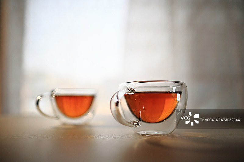 桌上双层水晶杯茶饮，背景为窗帘与自然光图片素材