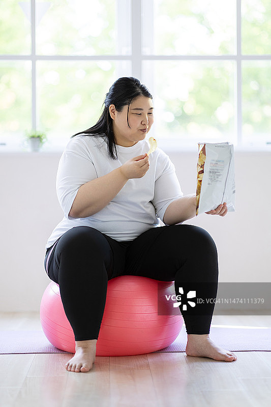 女人坐在平衡球上吃零食图片素材
