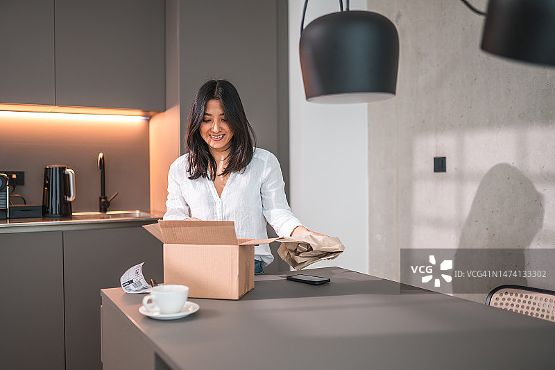 漂亮的亚洲年轻女人在家中打开纸箱图片素材