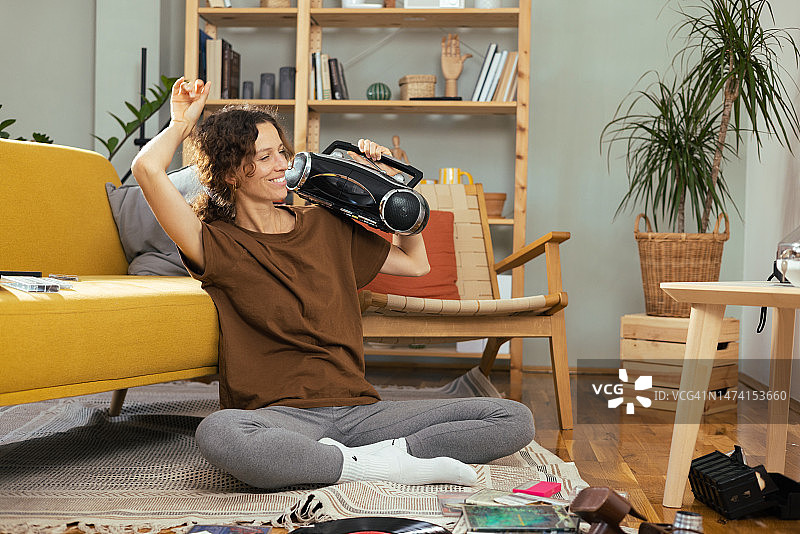 快乐的年轻女人在家中享受乐趣，用旧便携式音响听音乐图片素材
