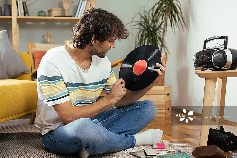 年轻男人在家欣赏旧音乐唱片和磁带的肖像图片素材