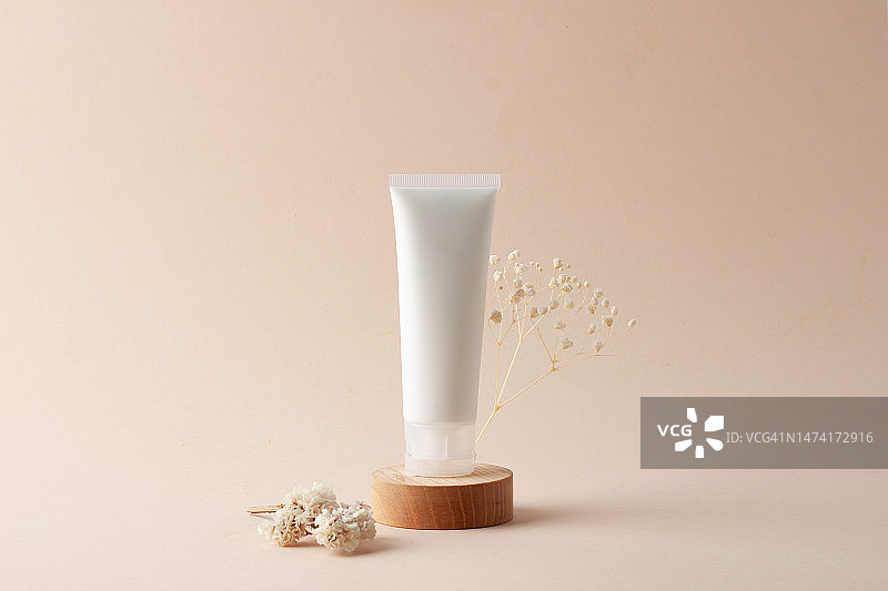 罗马尼亚：米色背景木质展台上带鲜花的化妆霜白色软管图片素材