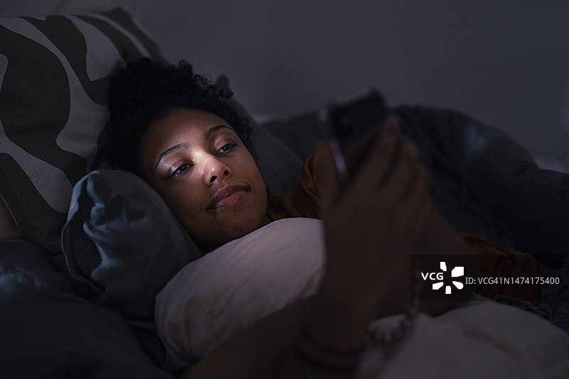 在床上使用手机的年轻微笑女人图片素材