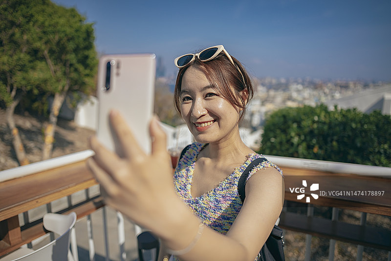 亚洲女性到旅游景点旅行，使用智能手机记录旅行记忆，并上传到社交媒体平台分享图片素材