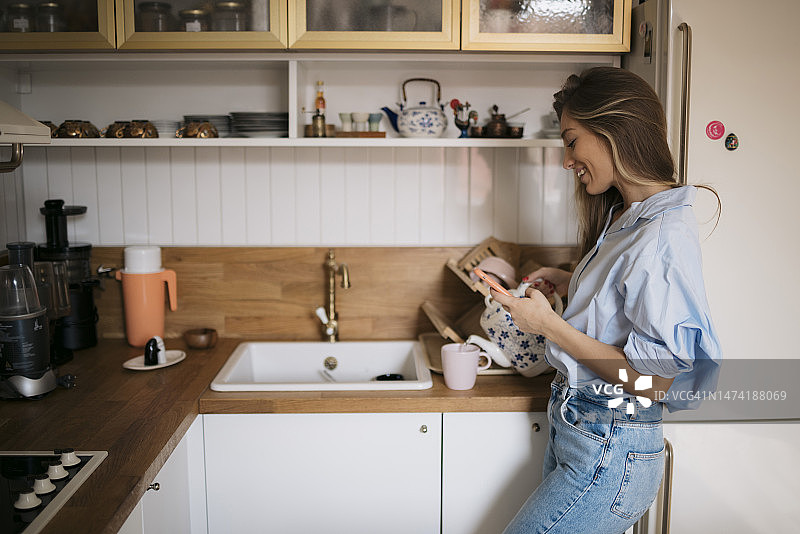 年轻女人在厨房使用手机图片素材