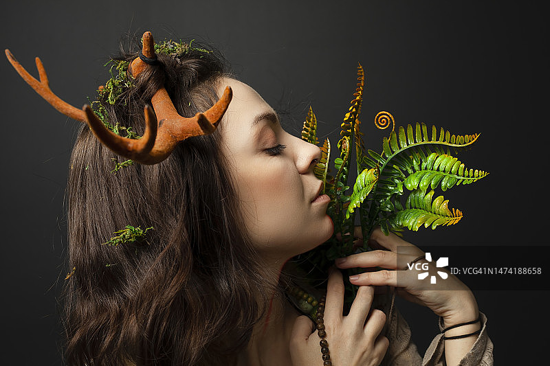 一个长着角的女德鲁伊或萨满的肖像，她手里拿着神奇的草药或植物，背景是黑色的。自然灵性，萨满教，草药学，仪式实践，神话象征。图片素材