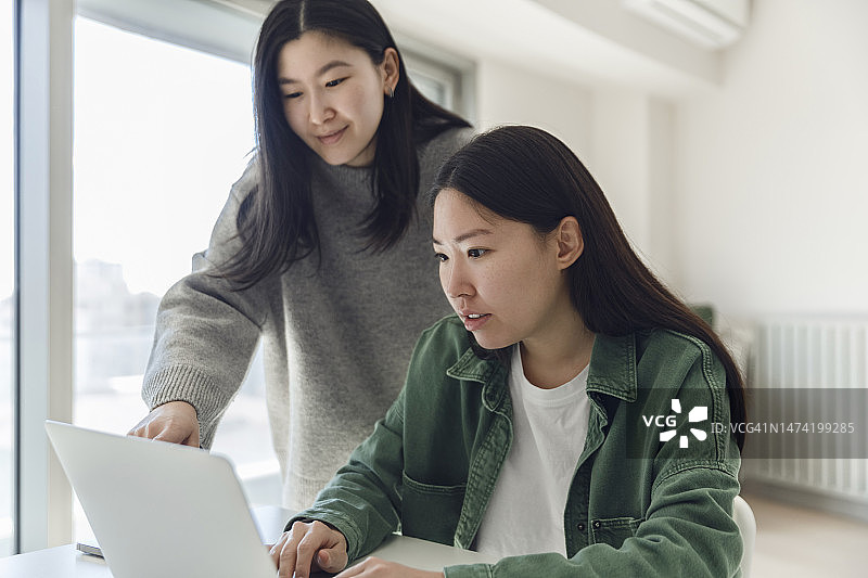 年轻女子帮助姐姐使用笔记本电脑工作图片素材