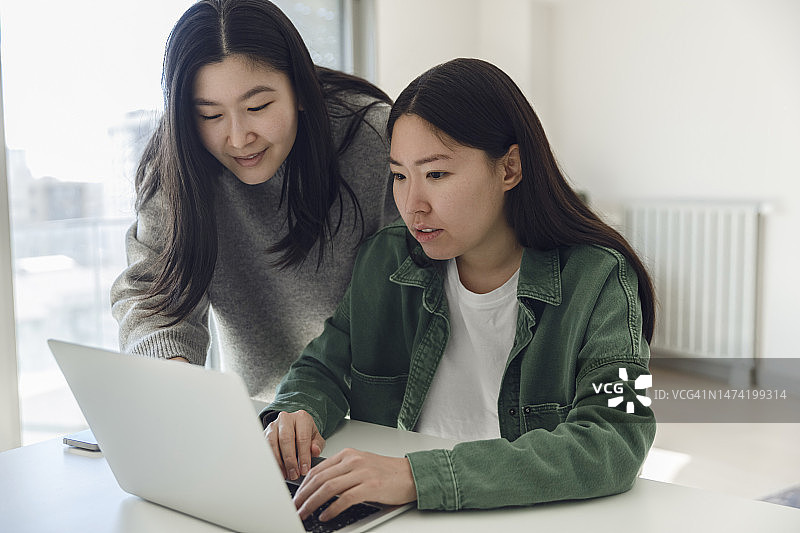 年轻女子帮助姐姐使用笔记本电脑工作图片素材