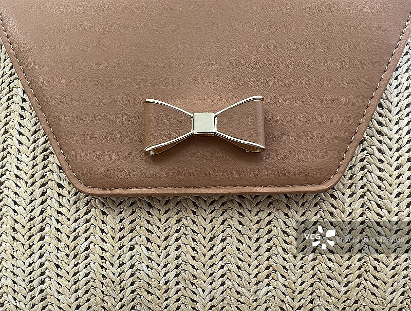 棕色人造革翻盖上的蝴蝶结装饰草编手提包图片素材