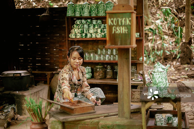 身穿卡巴雅服饰的亚洲女孩在爪哇老式公共厨房用石臼制作凉茶图片素材