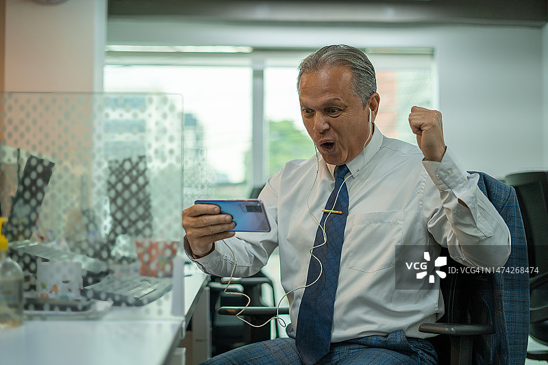 中年拉丁男人在办公室用手机观看比赛并举手庆祝图片素材