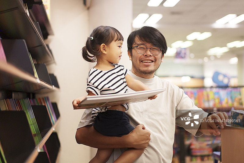 周末亲子时光：亚洲父亲与女儿一起选购书籍图片素材
