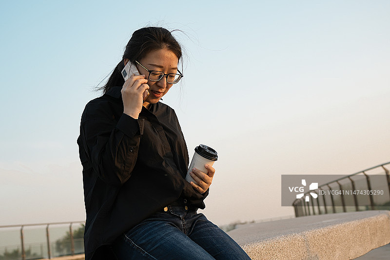 手拿咖啡和手机的商务女性在户外图片素材