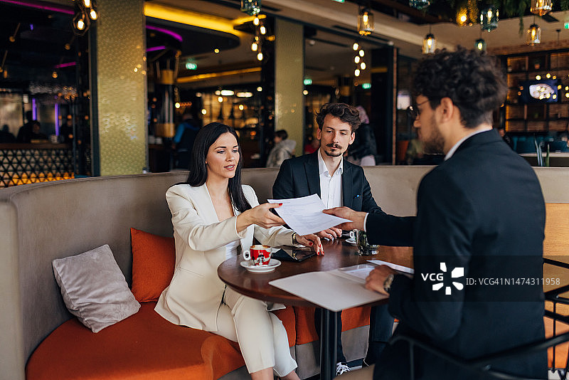 男候选人将简历交给两位正在面试他的企业家，应聘公司新职位图片素材