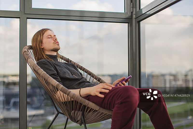 在阳台上手持手机的金发男人图片素材