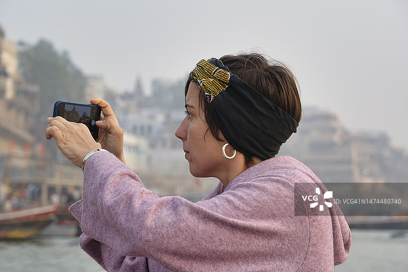早上，女游客在船上拍摄恒河/ गंगा河的 घाट 照片图片素材
