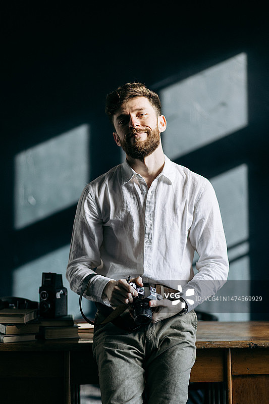 摄影棚里拿着相机的快乐英俊男人图片素材