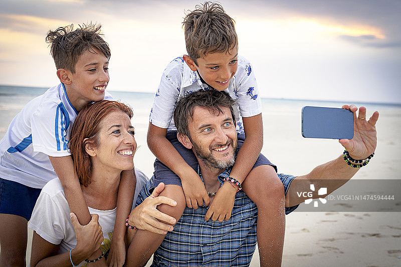 幸福的家庭在海滩上用智能手机自拍图片素材