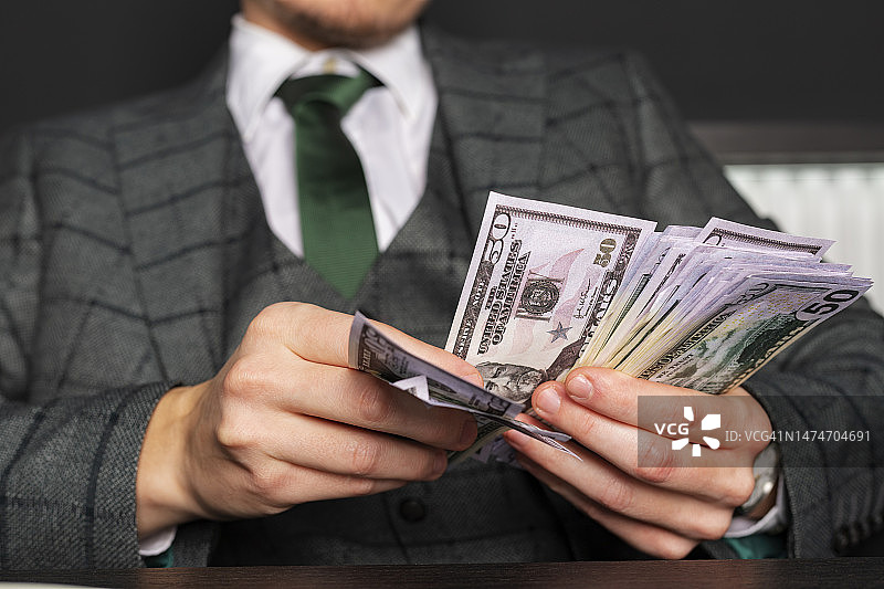 穿着灰色正装戴眼镜的年轻男子坐在办公桌前数钱，商人拿着钱图片素材