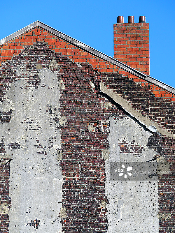 布鲁塞尔一栋风化棕色砖房的山墙，带有灰色水泥、瓦屋顶、烟囱和蓝色天空图片素材