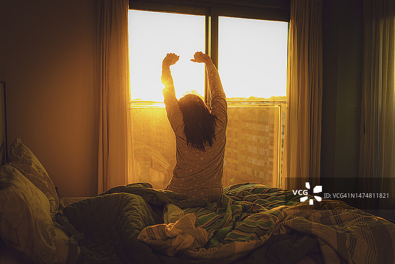 清晨，透过窗户伸展双臂的女人图片素材