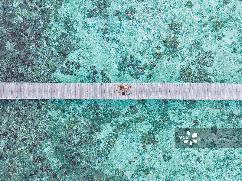 情侣躺在珊瑚礁木板路上的航拍图片素材