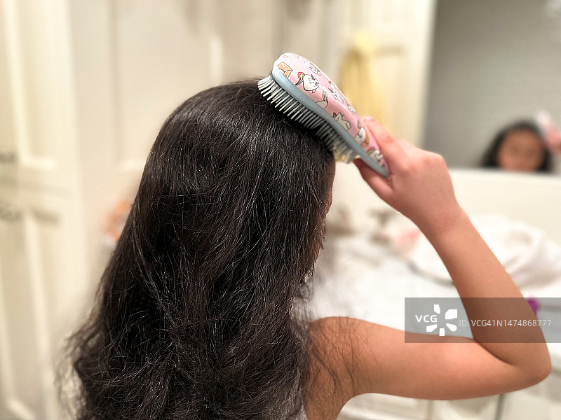 混血女孩站在浴室镜子前刷头发图片素材