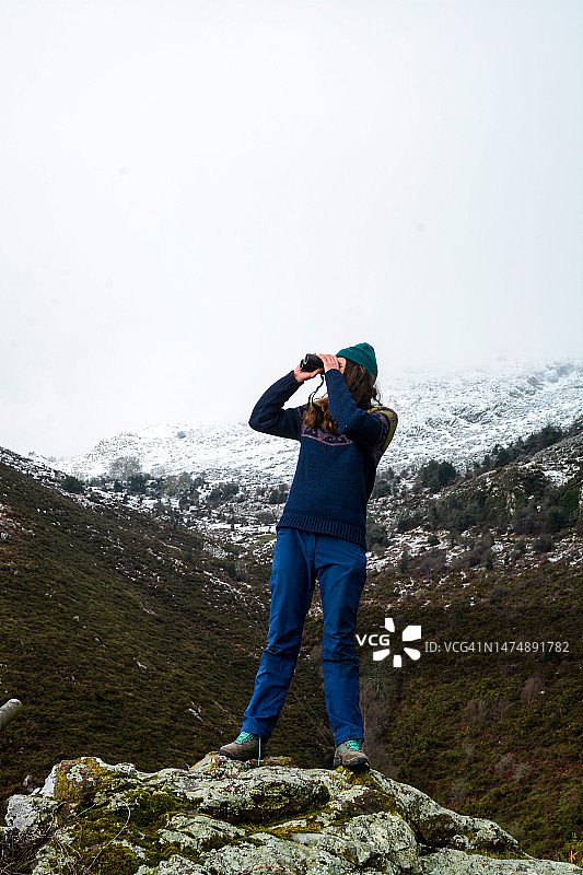 身穿冬装的年轻女子在山区用双筒望远镜观察图片素材